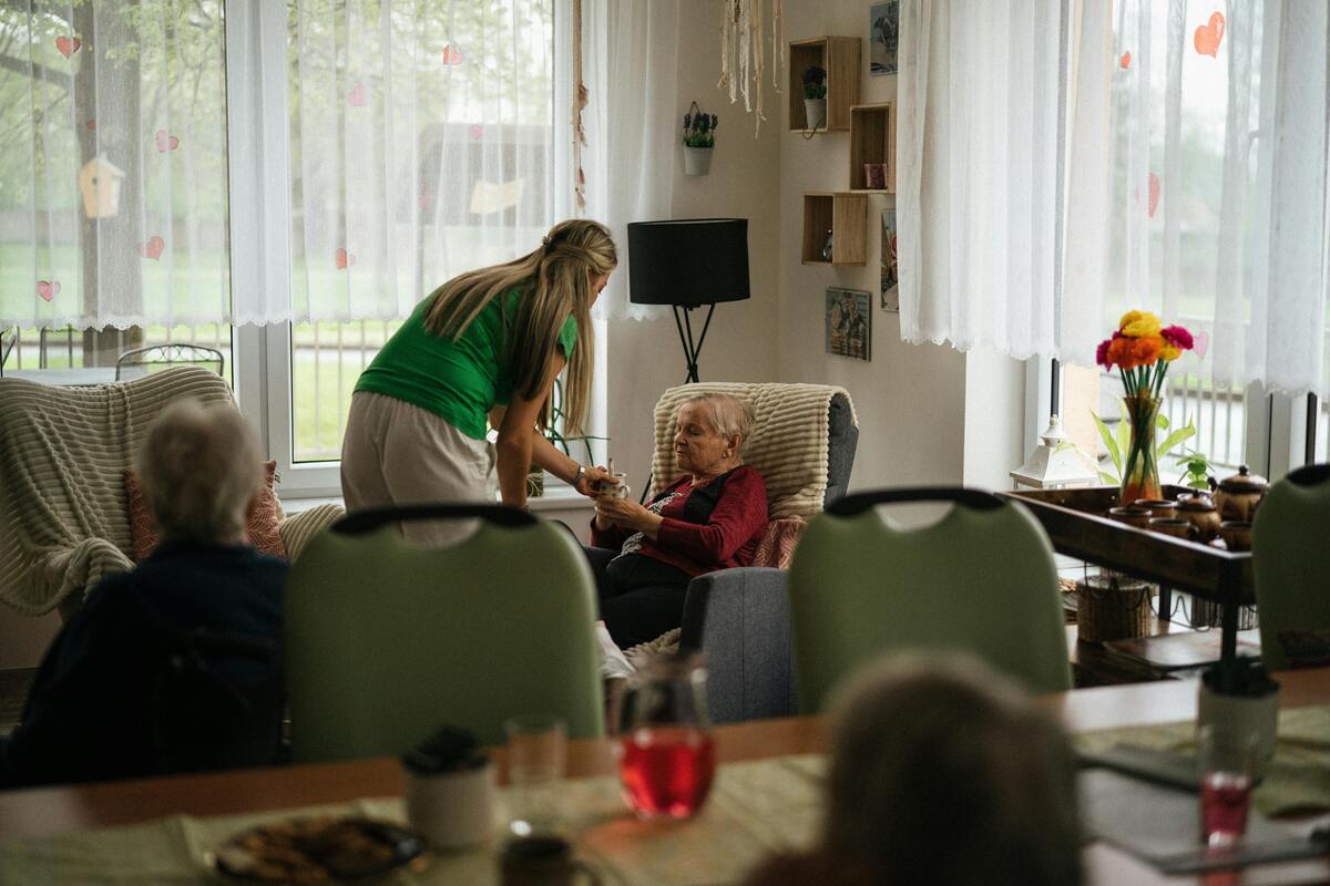 pečující v domově podává sklenici vody seniorce