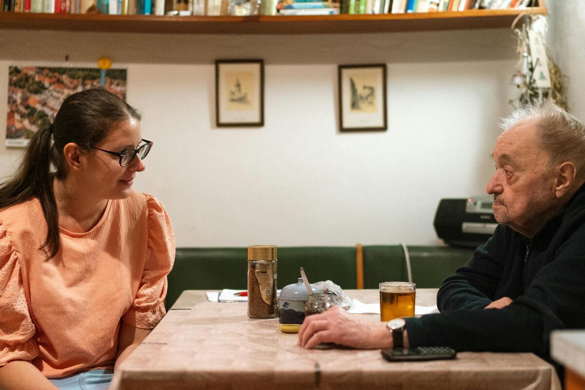 vnučka sedí s dědečkem u stolu a povídají si