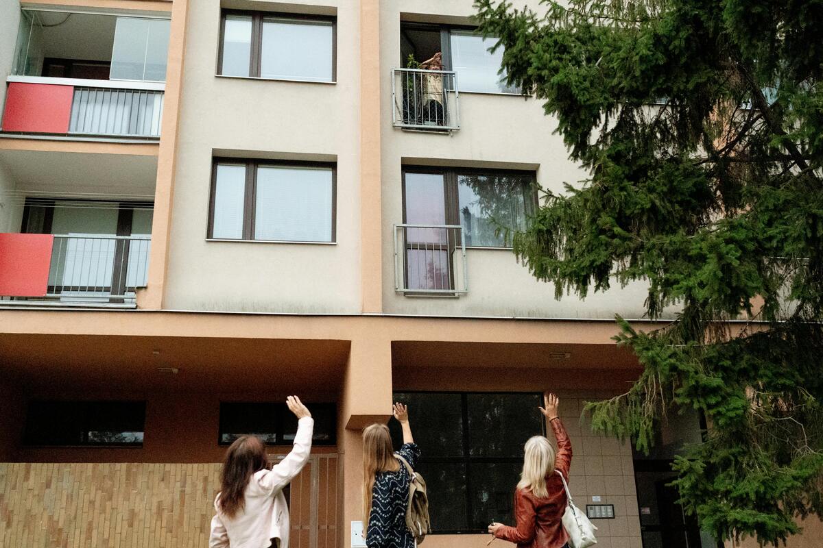 ženy pečovatelky mávají seniorce do okna