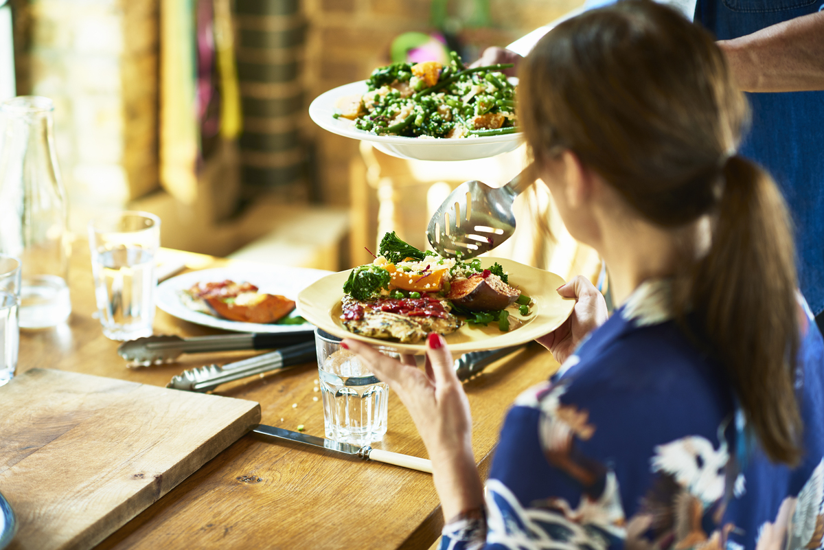 žena sedící u stolu drží v rukou talíř a dostává na něj velmi lákavě vypadající zdravý letní oběd