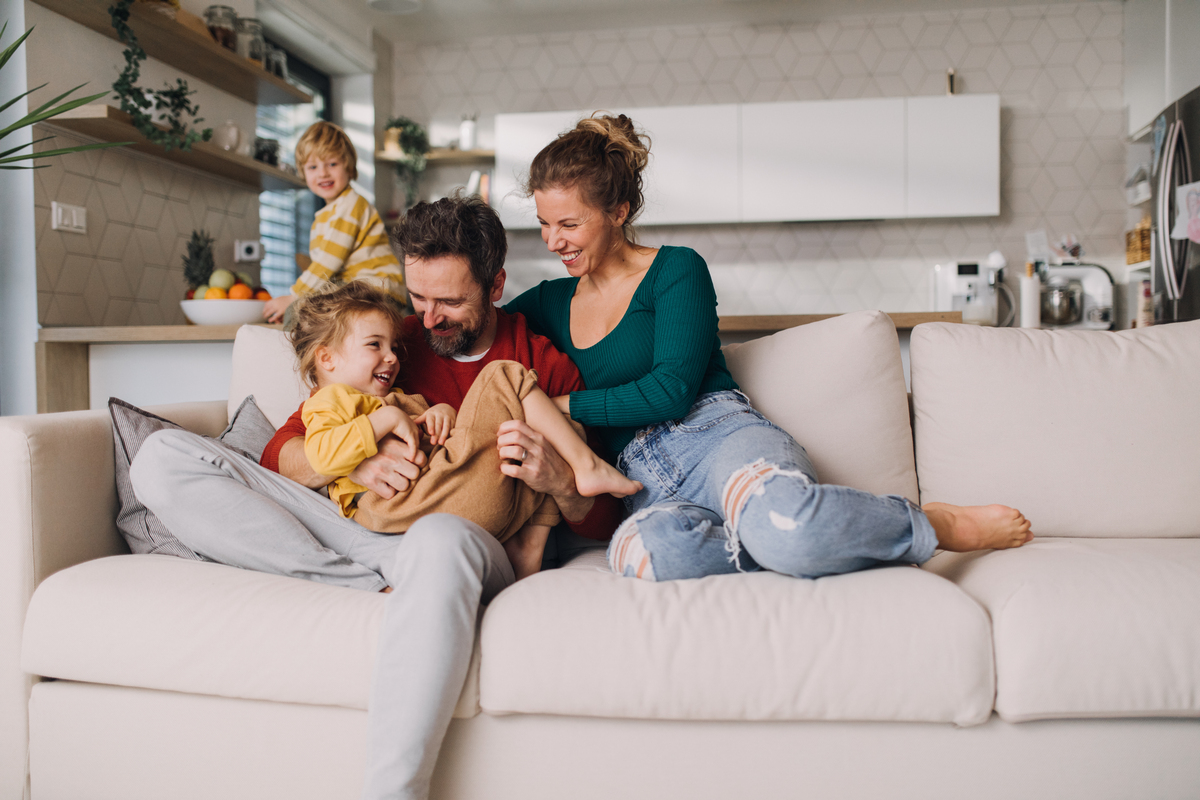 rodiče objímají jedno dítě na gauči a druhé se na ě usmívá z povzdálí