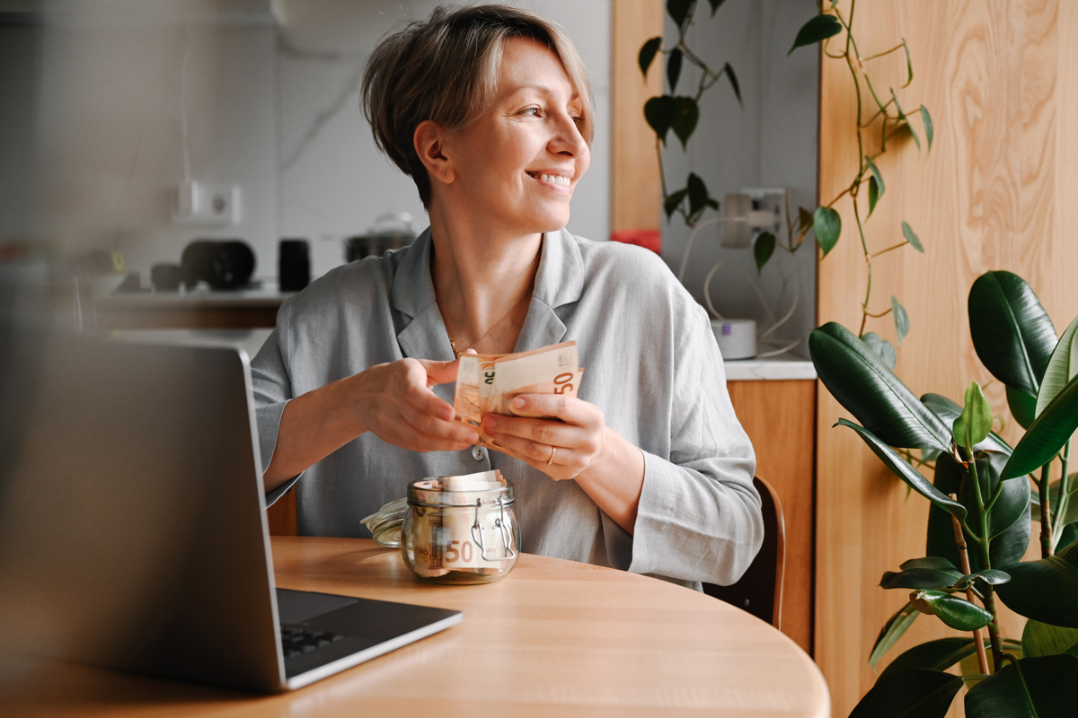 žena sedící u počítače s bankovkami v ruce je ráda, že udělala investiční rozhodnutí, které se jí vyplatilo