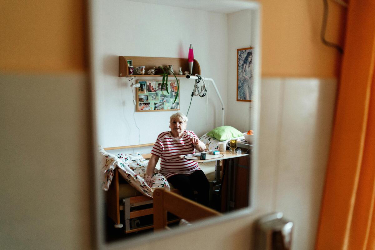 seniorka ubytovaná v zařízení pro seniory sedí na posteli